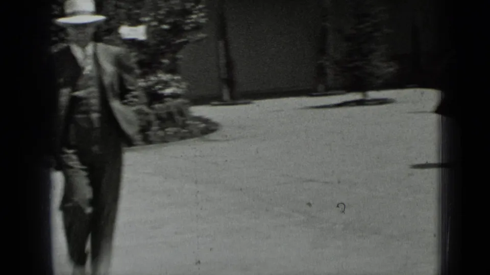 In 1937 San Francisco home-movie footage, a man in a suit and fedora walks through a sunlit garden courtyard.