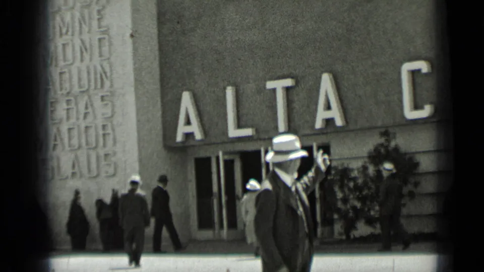 1937 San Francisco frame with a man in a white hat pointing near the ALTA facade while other adults walk nearby.
