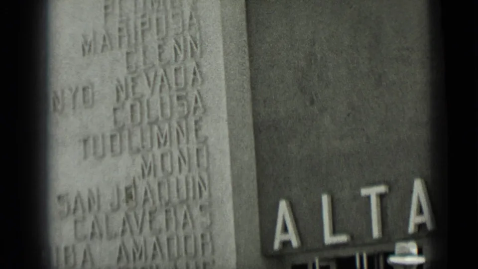 1937 San Francisco close framing of carved place names on a facade with partial ALTA lettering and the brim of a white hat at lower edge.