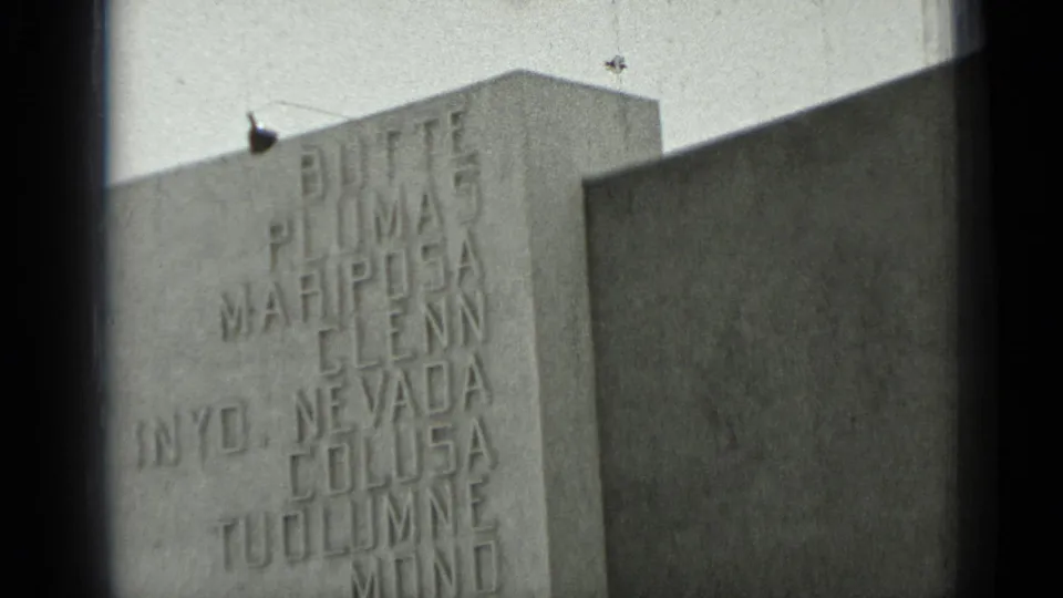 1937 San Francisco 8mm frame showing a close view of a blocky stone wall engraved with names including Butte, Plumas, and Nevada.