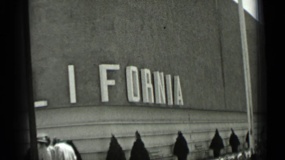 1937 San Francisco frame showing partial CALIFORNIA facade lettering, a small group below, shrubs, and the edge of a flag.