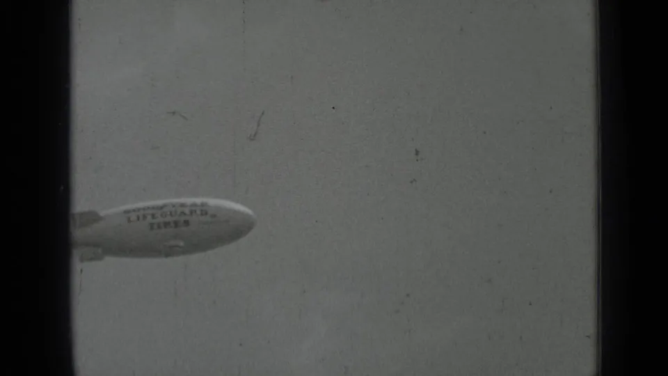 The branded blimp is partly cropped as it moves through the cloudy San Francisco sky in grainy 1937 8mm footage.