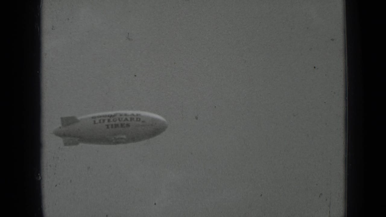 Goodyear blimp with Lifeguard Tires lettering drifting across a pale sky.