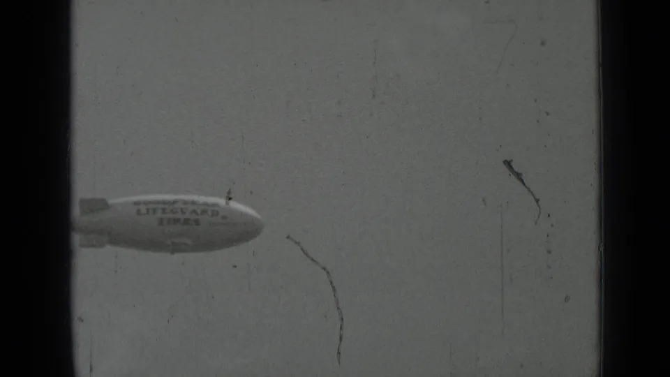 1937 San Francisco 8mm frame with the Goodyear Lifeguard Tires blimp near the upper sky, softened by film grain and scratches.