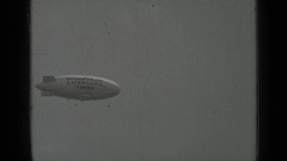 1937 San Francisco 8mm frame showing the Goodyear Lifeguard Tires blimp lower in the pale sky with visible archival grain.