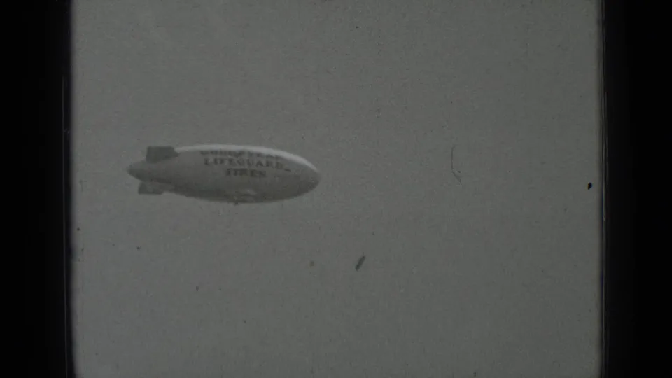 1937 San Francisco 8mm frame with the distant Goodyear Lifeguard Tires blimp centered low against a pale, worn film image.