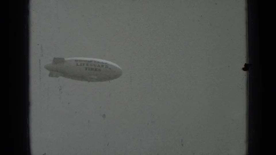 1937 San Francisco home-movie frame showing a Goodyear blimp advertising Lifeguard Tires against a pale sky.
