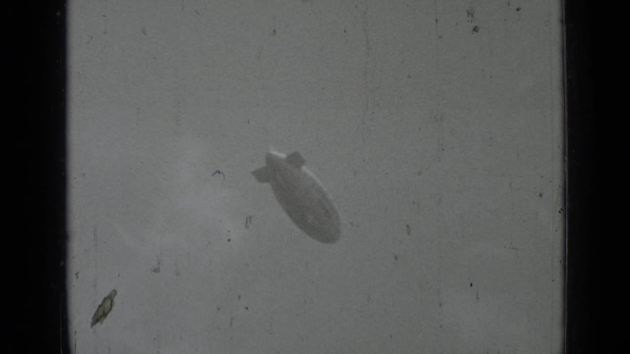 Distant blimp angled in a pale sky with heavy film borders.