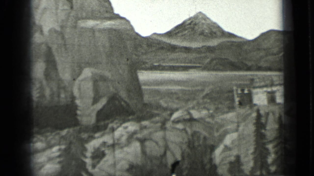 Painted mountain backdrop, lake area, rocks, and a small structure within a miniature set.