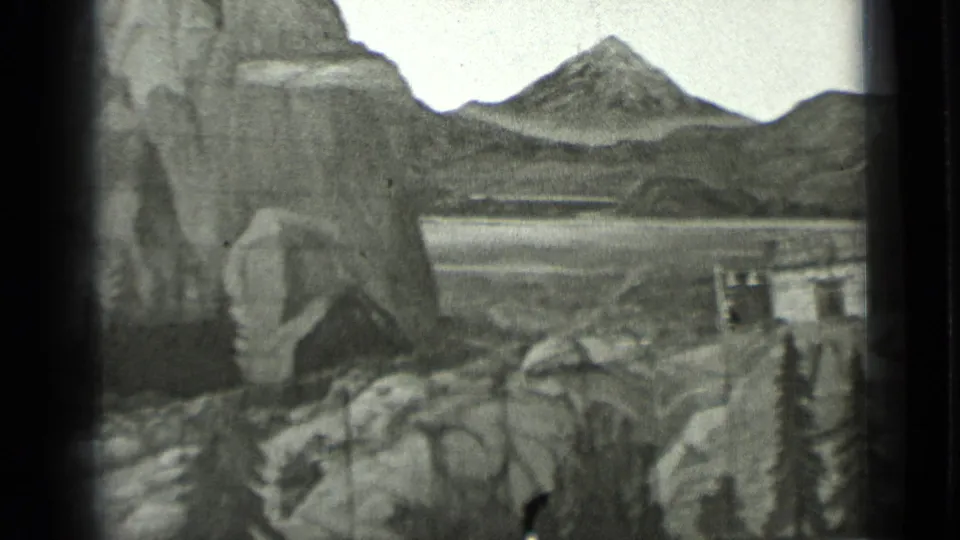 1937 San Francisco 8mm frame showing a miniature mountain-and-lake backdrop with rocky terrain and a small building on the right.