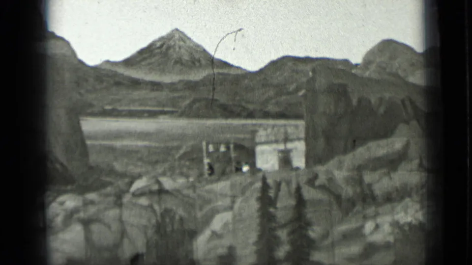 1937 San Francisco 8mm frame showing a staged mountain landscape with a small building and a tiny human figure for scale.