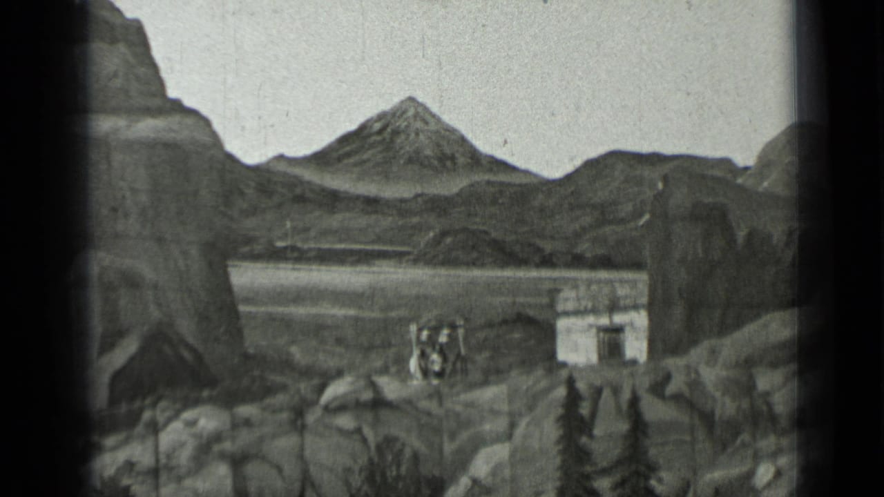 Distant performers stand near a small structure in a rocky mountain set.