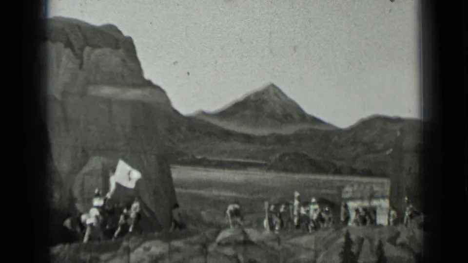 1937 8mm frame showing a rider holding a flag at left while several groups of performers cross the rocky mountain set.