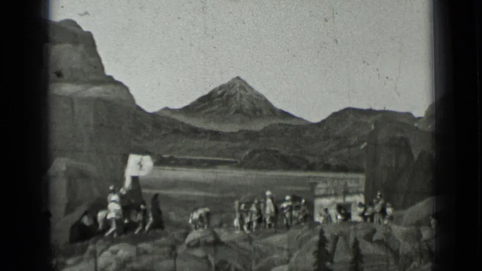 1937 8mm frame with a mounted flag bearer at left and multiple performers spread across a rocky set below the mountain backdrop.