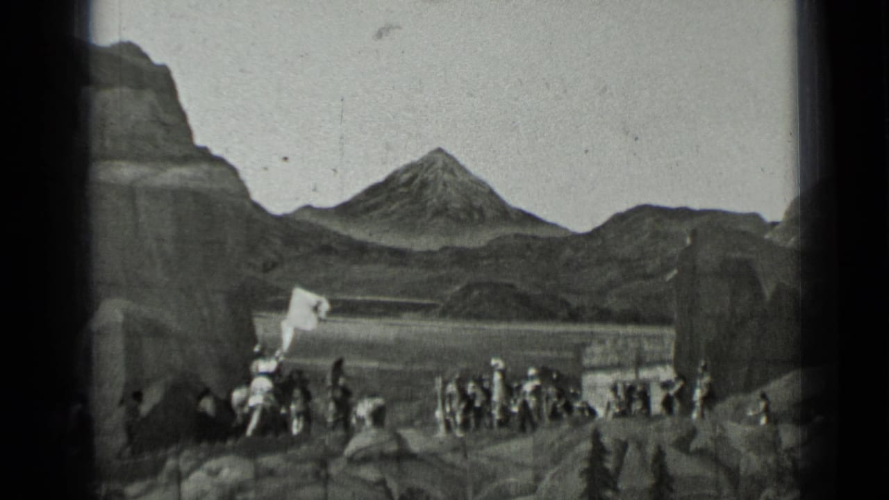 Uniformed men gather near rocks below a mountain backdrop with a white banner raised.