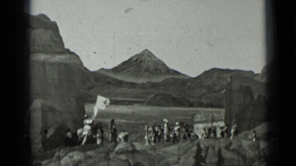 1937 black-and-white 8mm frame showing uniformed men gathered in a rocky mountain-themed setting with a white banner visible.