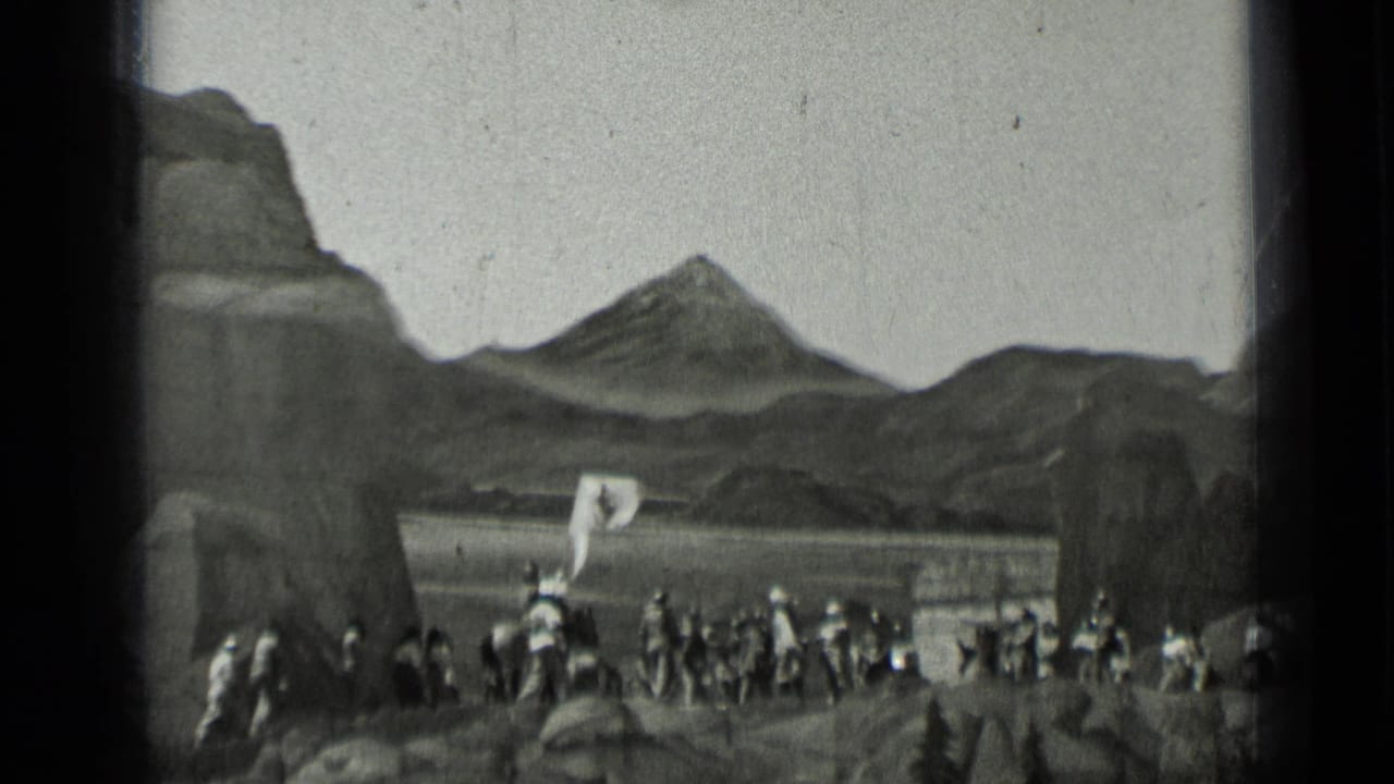 Group of men in dark uniforms stands across a rocky landscape with a peak behind them.