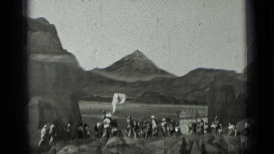 Black-and-white 1937 home-movie frame of a uniformed group spread across a rocky setting beneath a prominent mountain peak.