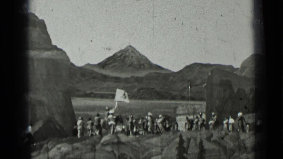 Black-and-white 1937 frame of a uniformed gathering in a rugged mountain-themed landscape, with a banner and pole at right.