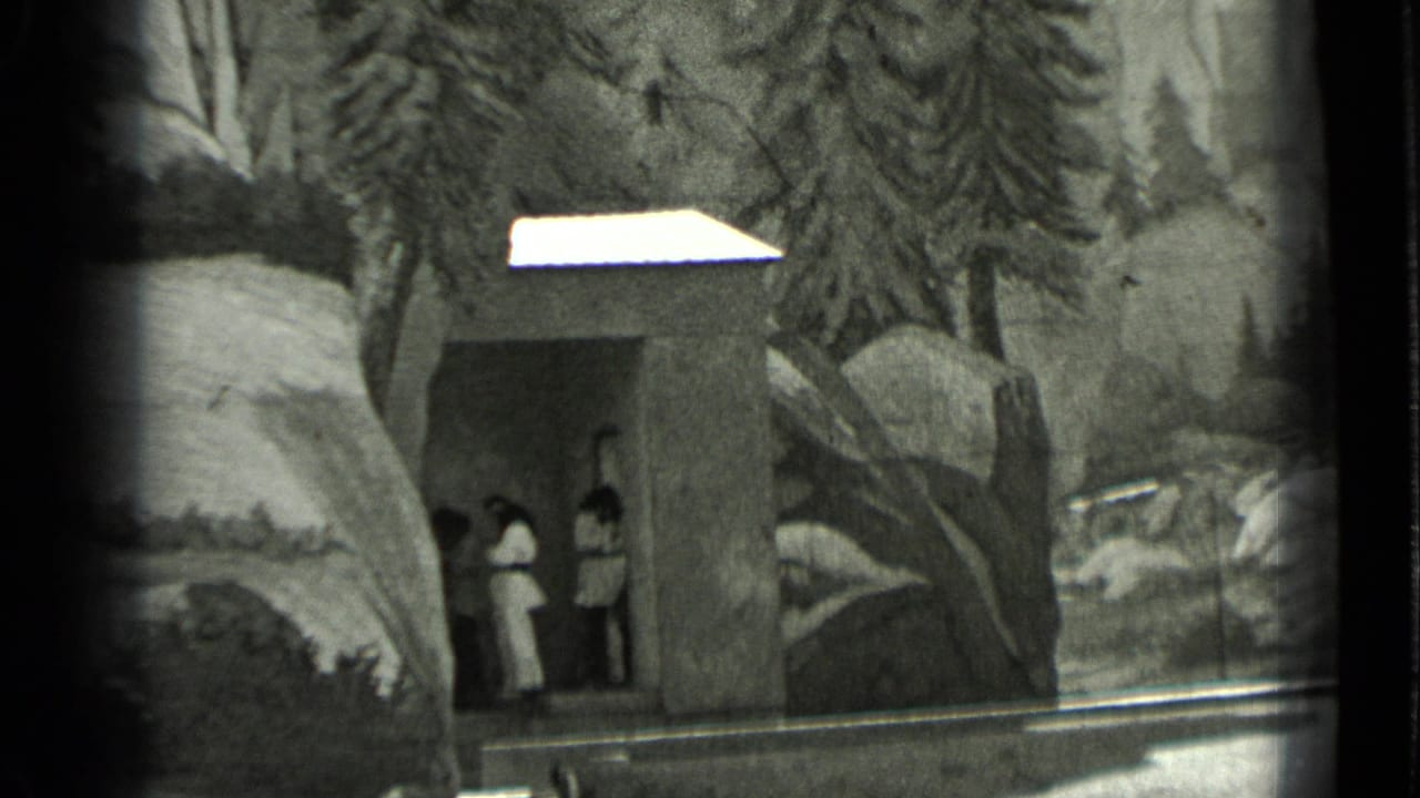 1937 San Francisco home-movie frame showing a small staged structure, rocky scenery, trees, and two visible performers or visitors.