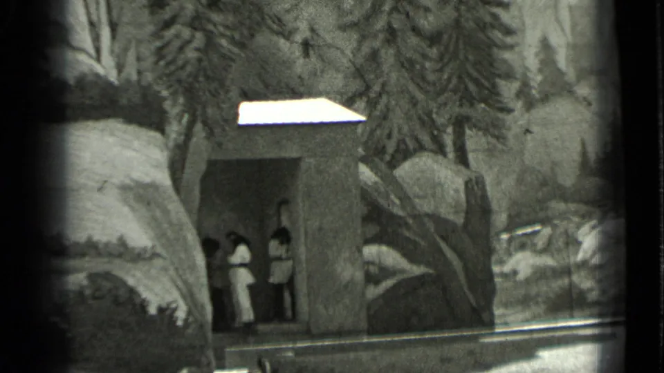 1937 San Francisco home-movie frame showing a small staged structure, rocky scenery, trees, and two visible performers or visitors.