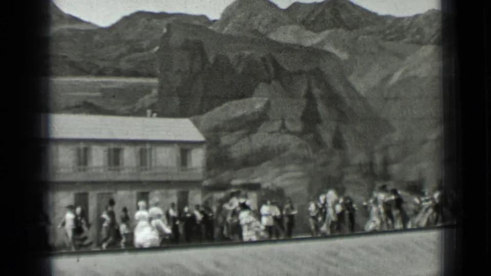 1937 San Francisco footage frame with a crowd moving in front of a long building, with mountainous scenery behind.