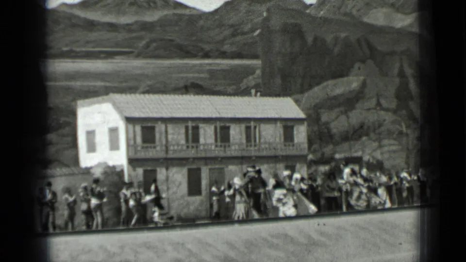 1937 San Francisco home-movie frame showing a social crowd in period clothing outside a large two-story building.