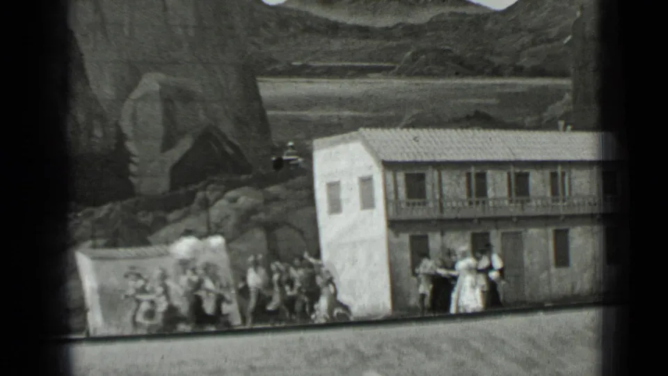 1937 San Francisco 8mm frame showing adults near a small staged building against a painted rocky backdrop.