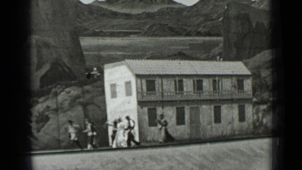 1937 San Francisco home-movie frame with adults walking near a small facade and scenic painted backdrop.