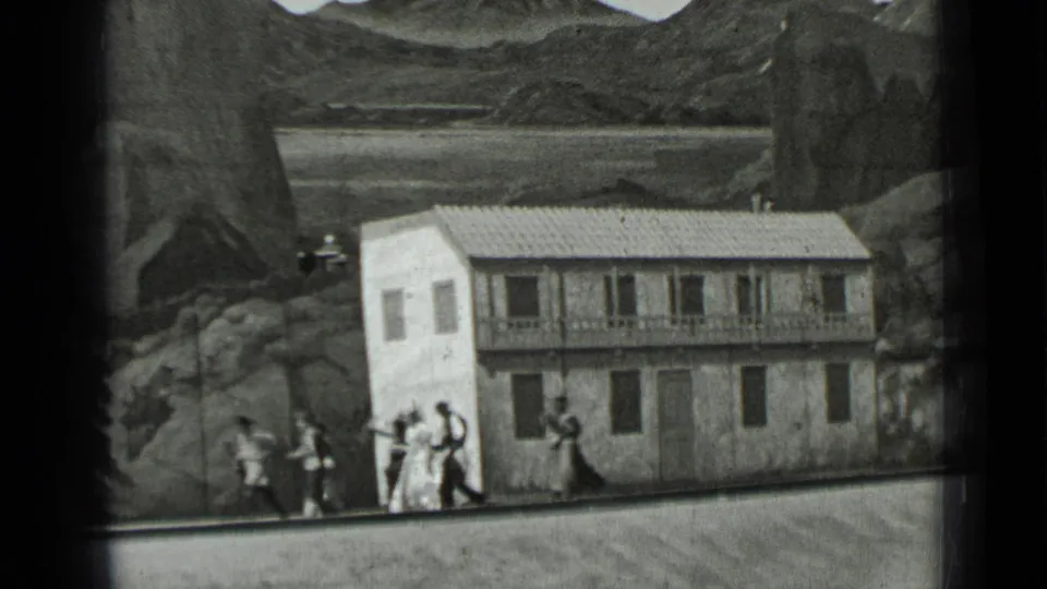 1937 San Francisco home-movie frame with adults walking near a small facade and scenic painted backdrop.