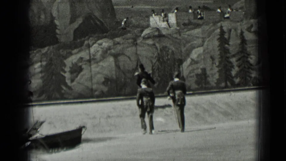Two dark-uniformed participants walk away from the camera before a painted rocky and forested backdrop in San Francisco footage dated 1937.