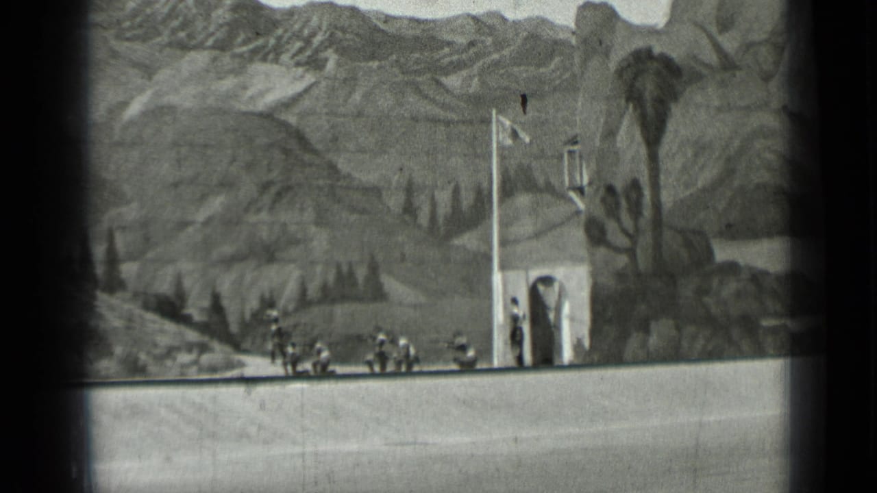 Uniformed figures march past a small set building in a rocky mountain scene.