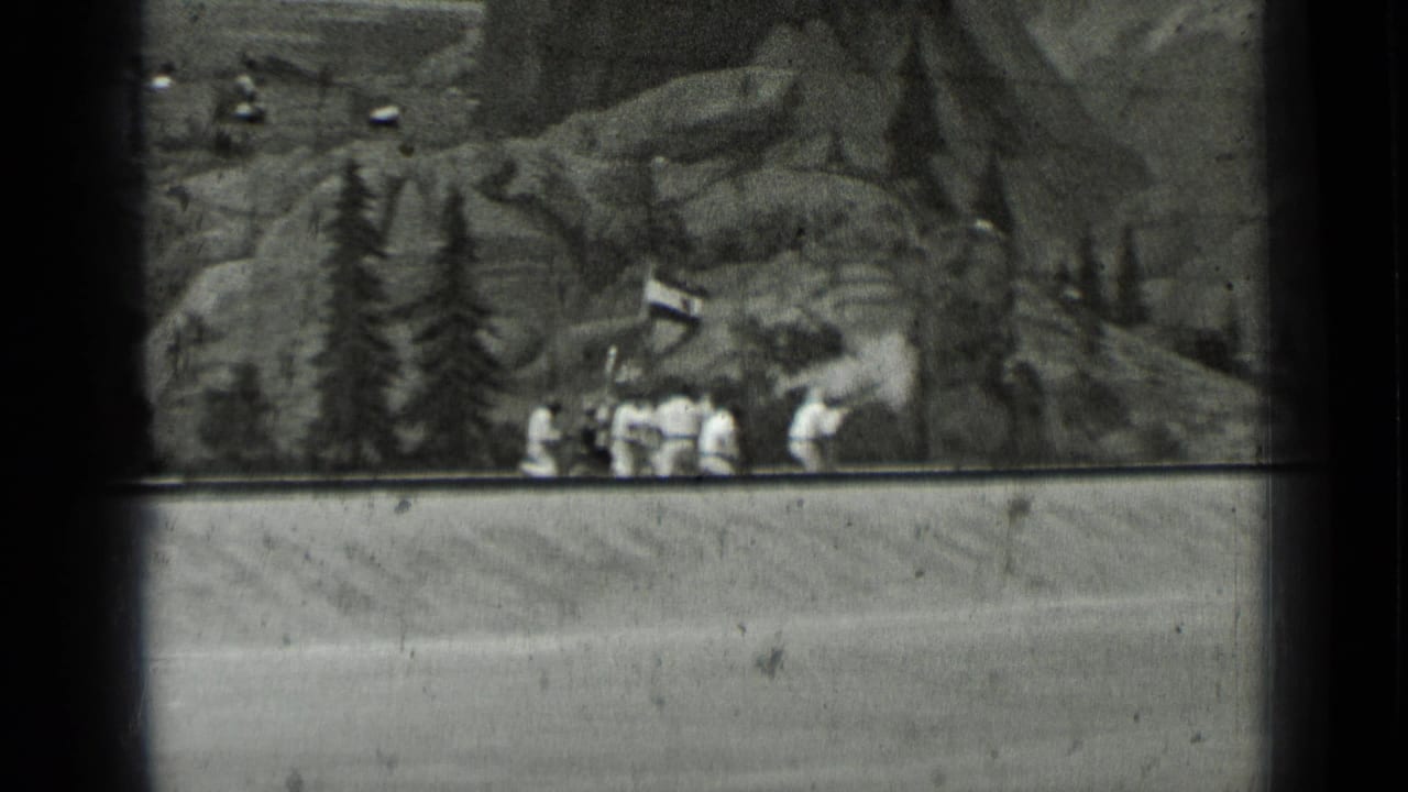 A group of uniformed figures gathers near trees and a small structure on a mountain set.
