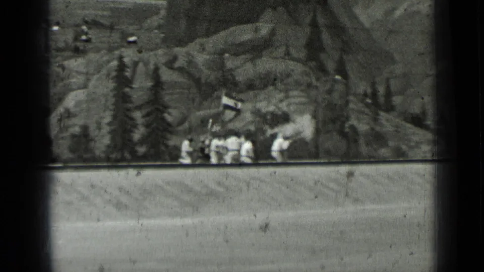 1937 San Francisco 8mm frame with uniformed figures near pine trees, a small structure and rocky painted scenery.