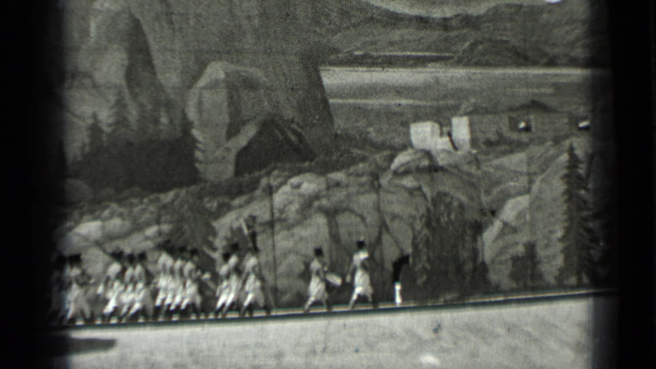 1937 San Francisco 8mm frame showing uniformed soldiers marching behind a drummer before a painted mountain scene.