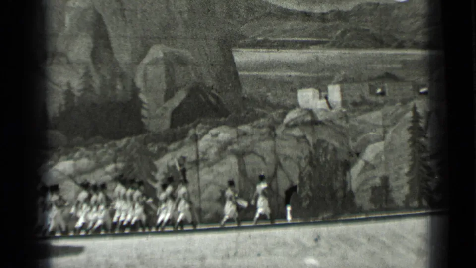 1937 San Francisco 8mm frame showing uniformed soldiers marching behind a drummer before a painted mountain scene.