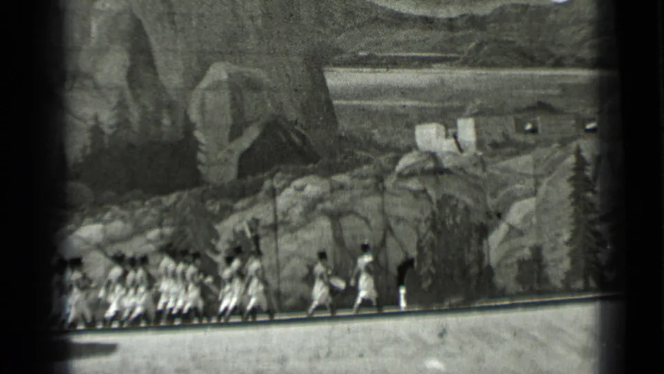 1937 San Francisco home-movie frame showing women moving in formation along a rocky path before a painted mountain scene.