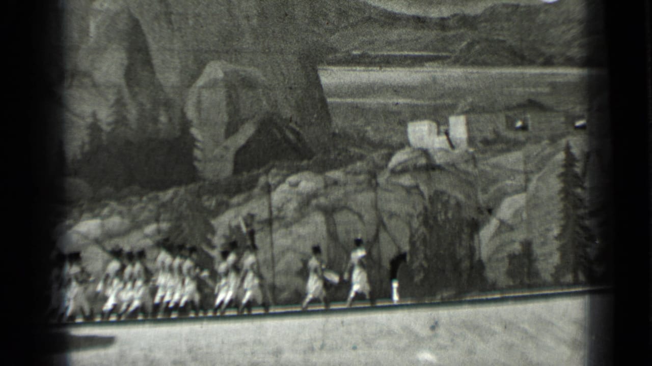 Costumed extras walk before a painted rocky backdrop with a small cabin shape.