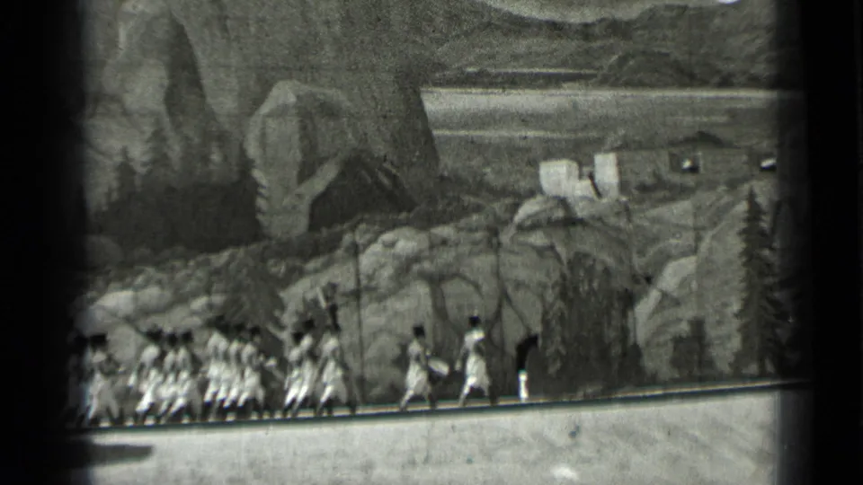 1937 8mm frame of extras crossing a studio set in San Francisco before painted mountain scenery and artificial shrubs.