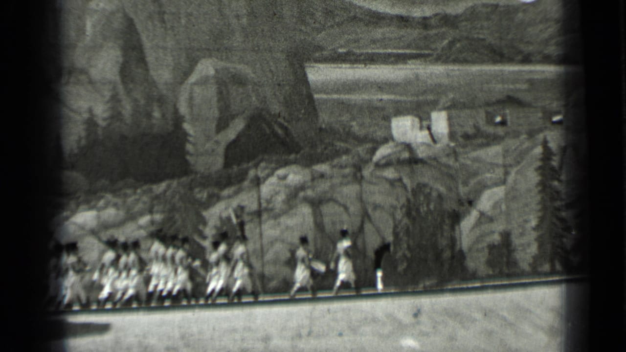 Extras continue walking along a set path below a painted mountain backdrop.