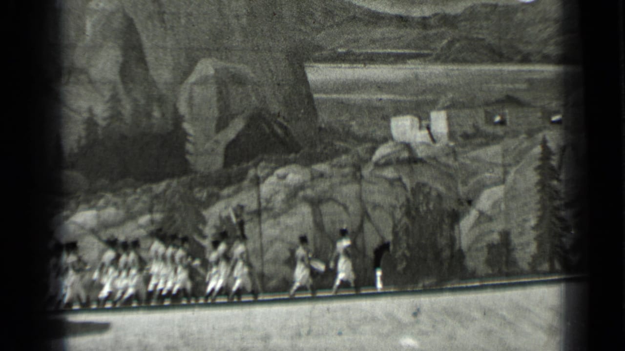 Uniformed group marches across a stage before a painted mountain backdrop.