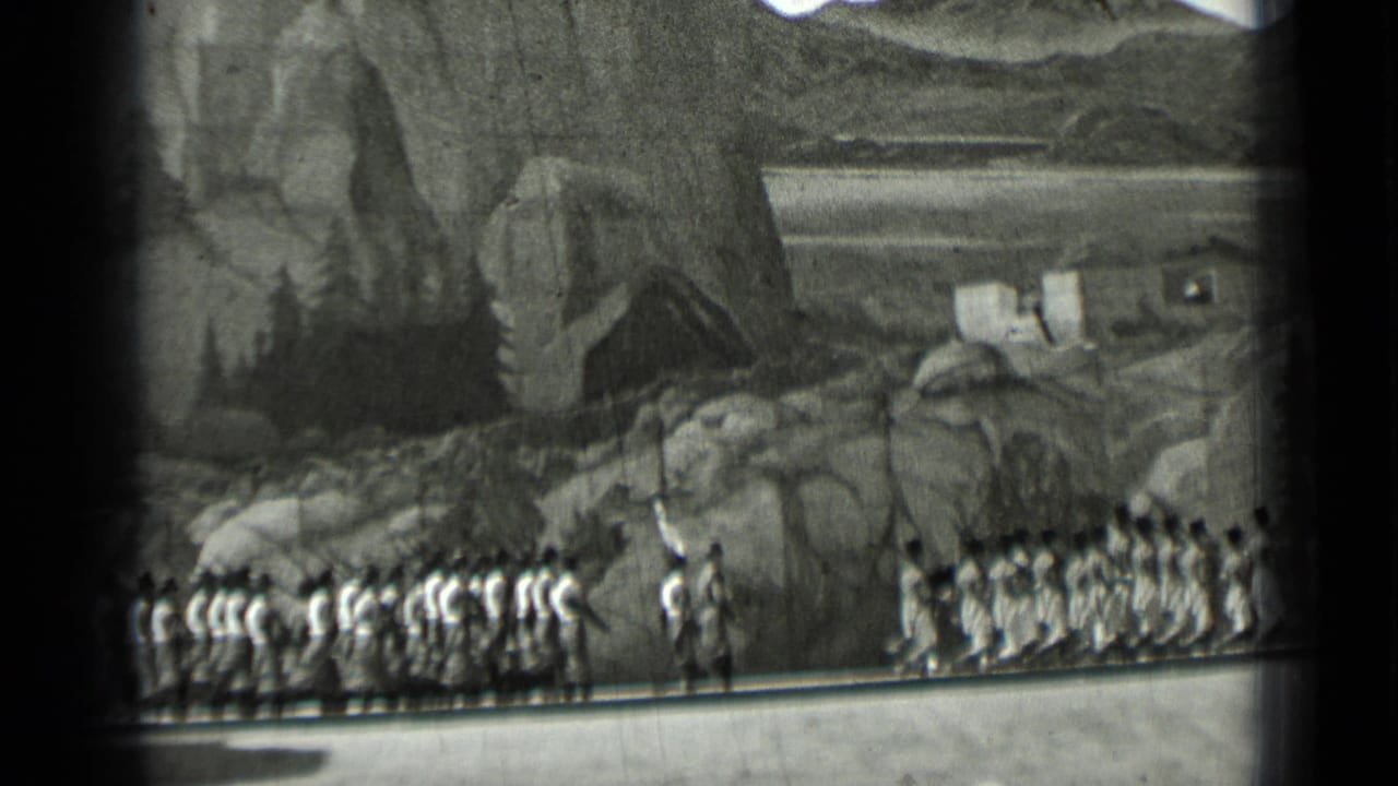 Uniformed marchers move in formation before rocky hillside scenery.