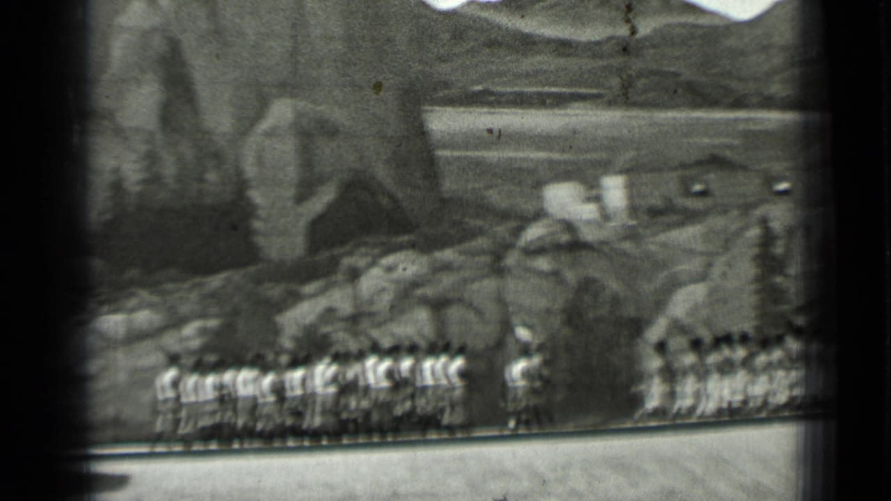 Rows of uniformed marchers continue across a rocky scenic background.