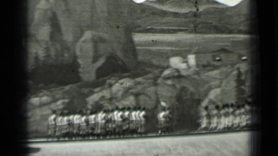 Uniformed participants march in rows across the frame, with rocky hillside scenery and trees behind them in 1937 San Francisco footage.