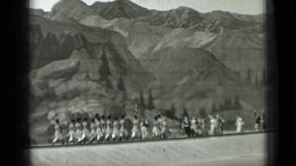1937 San Francisco 8mm frame showing costumed performers in a staged Western scene before rocky mountains and pine shapes.