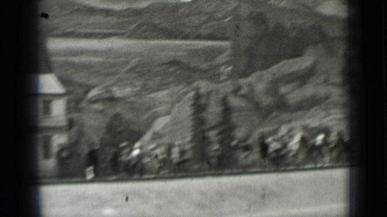 Distant riders and workers near rocky terrain with a small building at left.