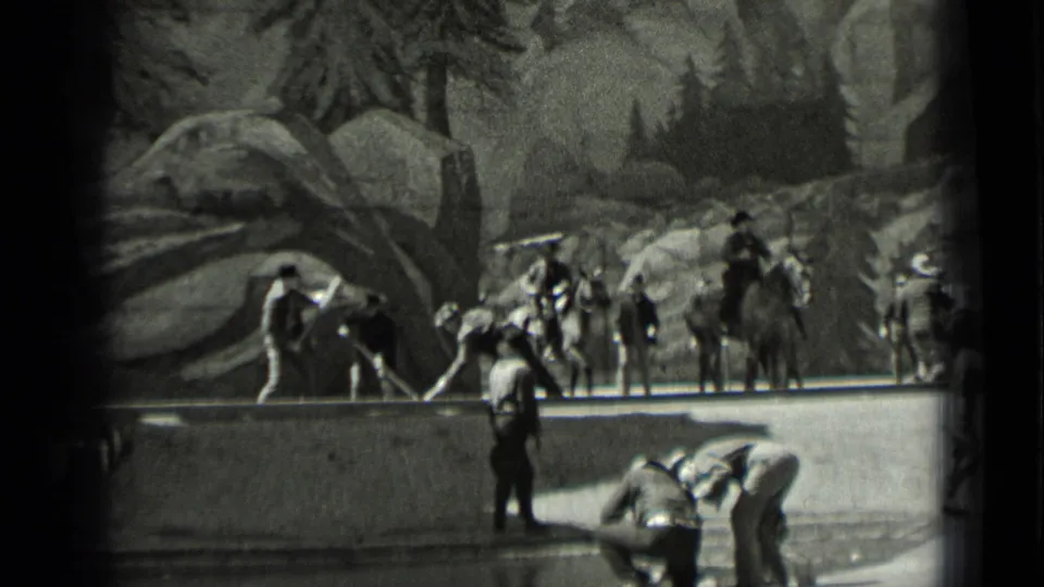 1937 San Francisco frame with horseback riders, standing workers, and crouching laborers beside a low edge in rocky terrain.