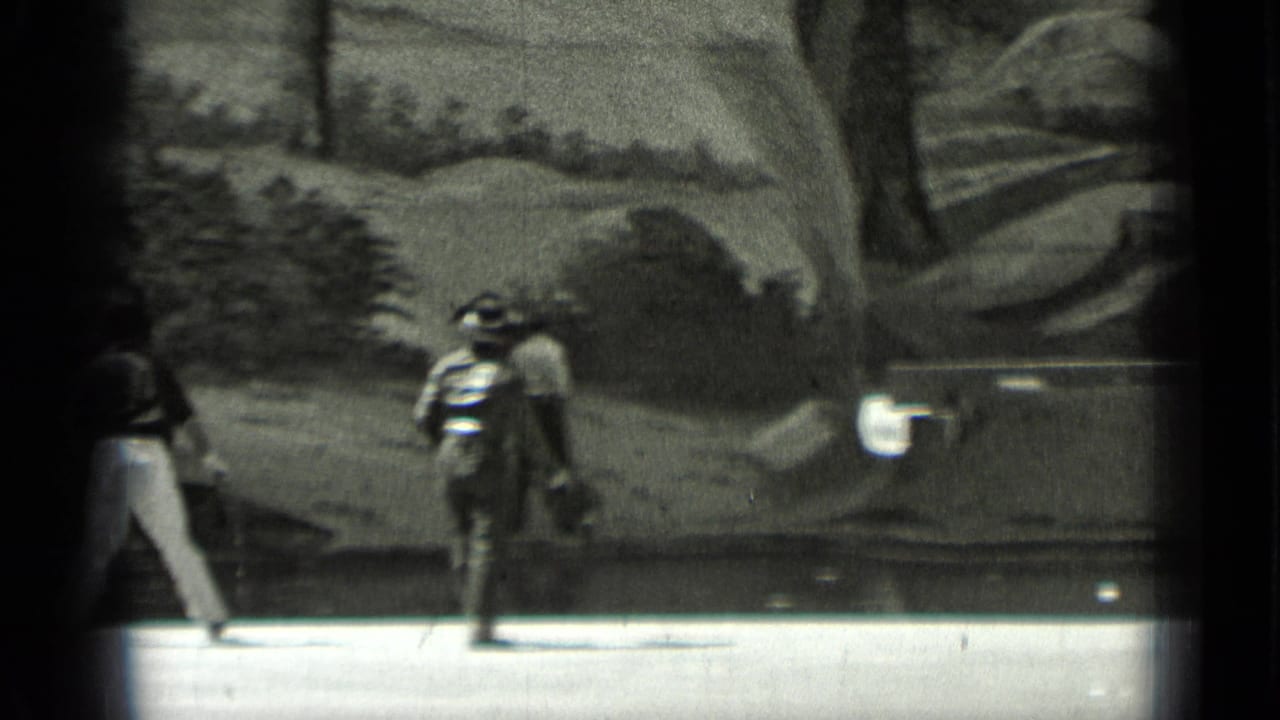 Two costumed figures walk past a painted scenic backdrop.