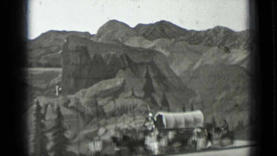 Costumed people gather near a covered wagon in front of painted hills and rocky scenery in the 1937 San Francisco home movie.