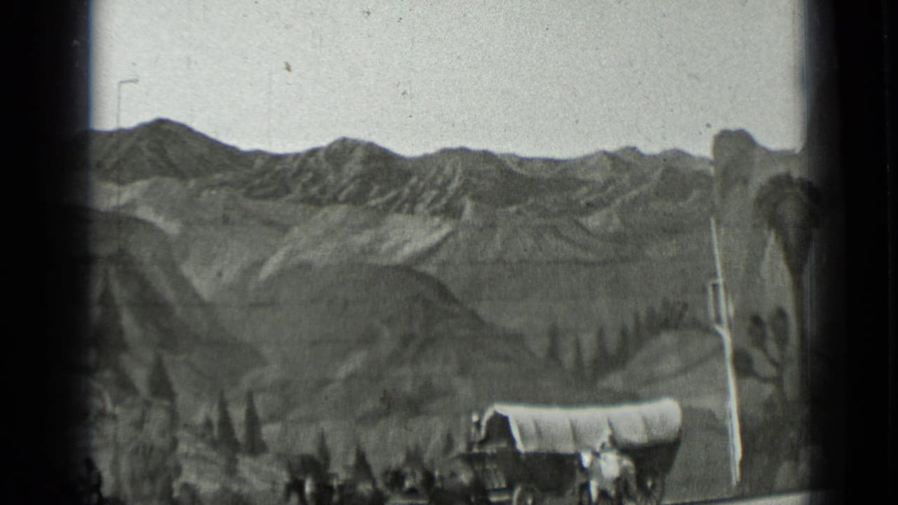 Covered wagon and painted mountain backdrop in a staged Western scene.